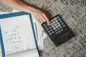 person typing on calculator with workings out for life insurance quotes next to them on the floor